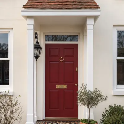 Deep red six-panel timber entrance door with brass knocker under a tiled porch