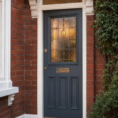 Dark grey timber entrance door with leaded stained glass panel on a red brick villa