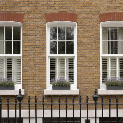 Three white timber sash windows with window boxes on a London brick terrace